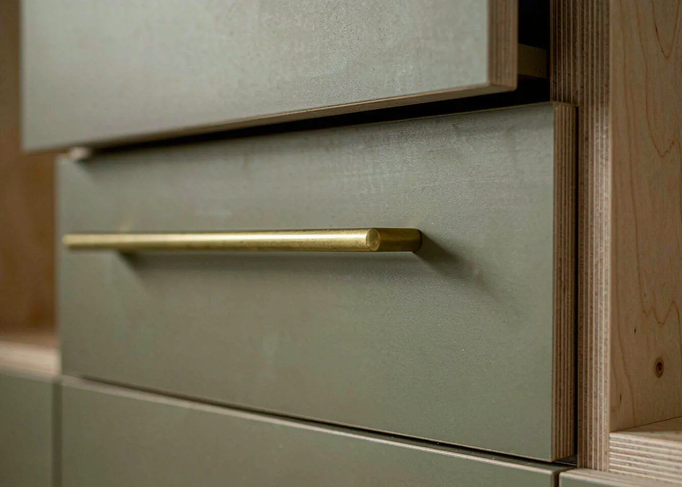 close-up of custom kitchen cabinet drawer with brushed brass handle and plywood edge