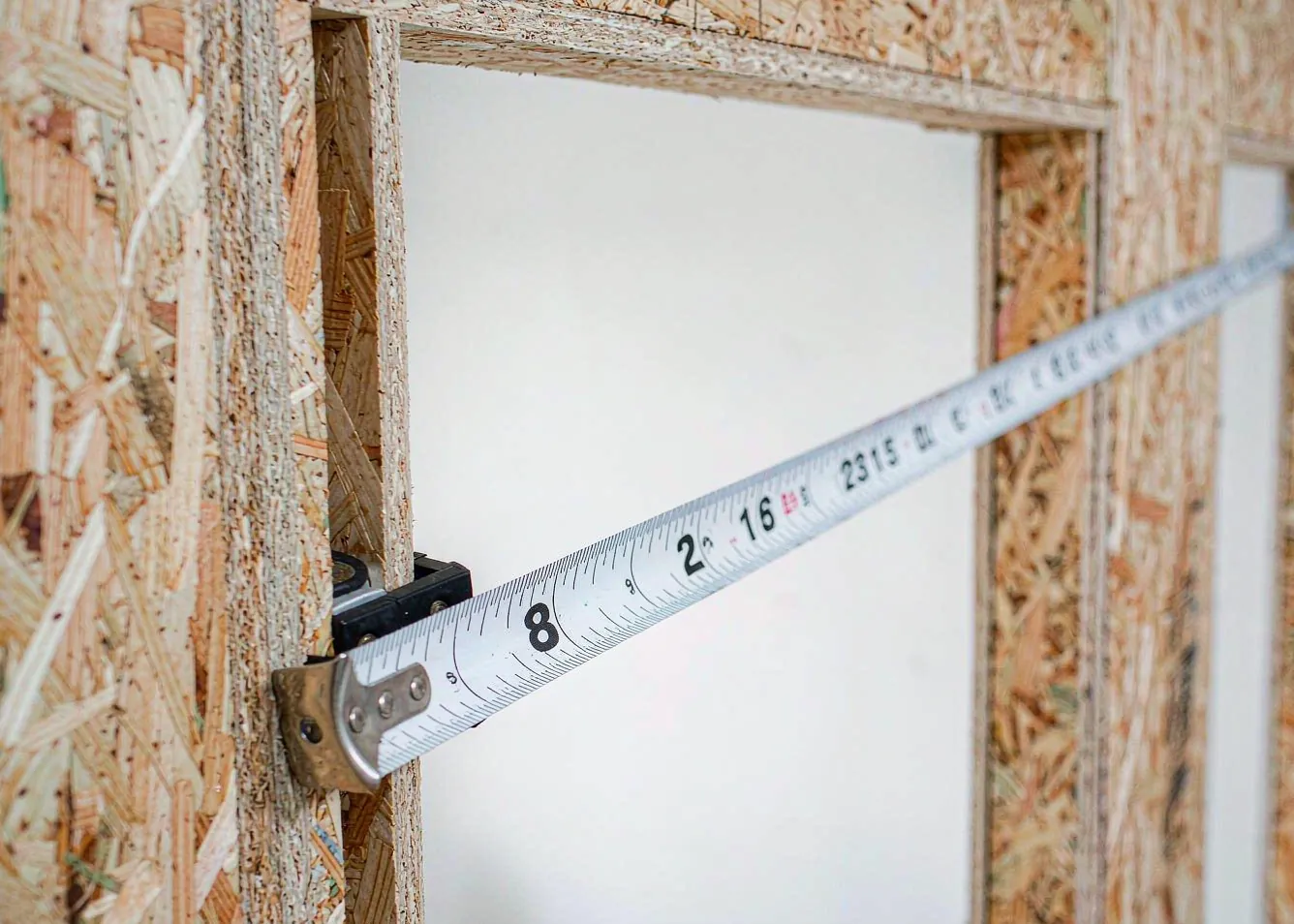 measuring door rough opening width on a wooden wall stud with a tape measure